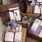 Closed wooden gift box with a purple ribbon, orchid flower and illustrated card beside an open box of gifts