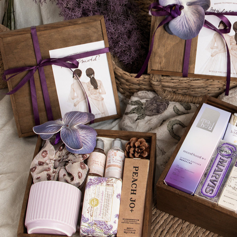 Closed wooden gift box with a purple ribbon, orchid flower and illustrated card beside an open box of gifts