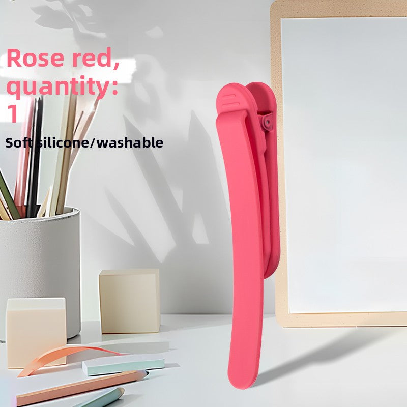 Single rose red silicone bookmark clip standing on a desk beside a pen cup