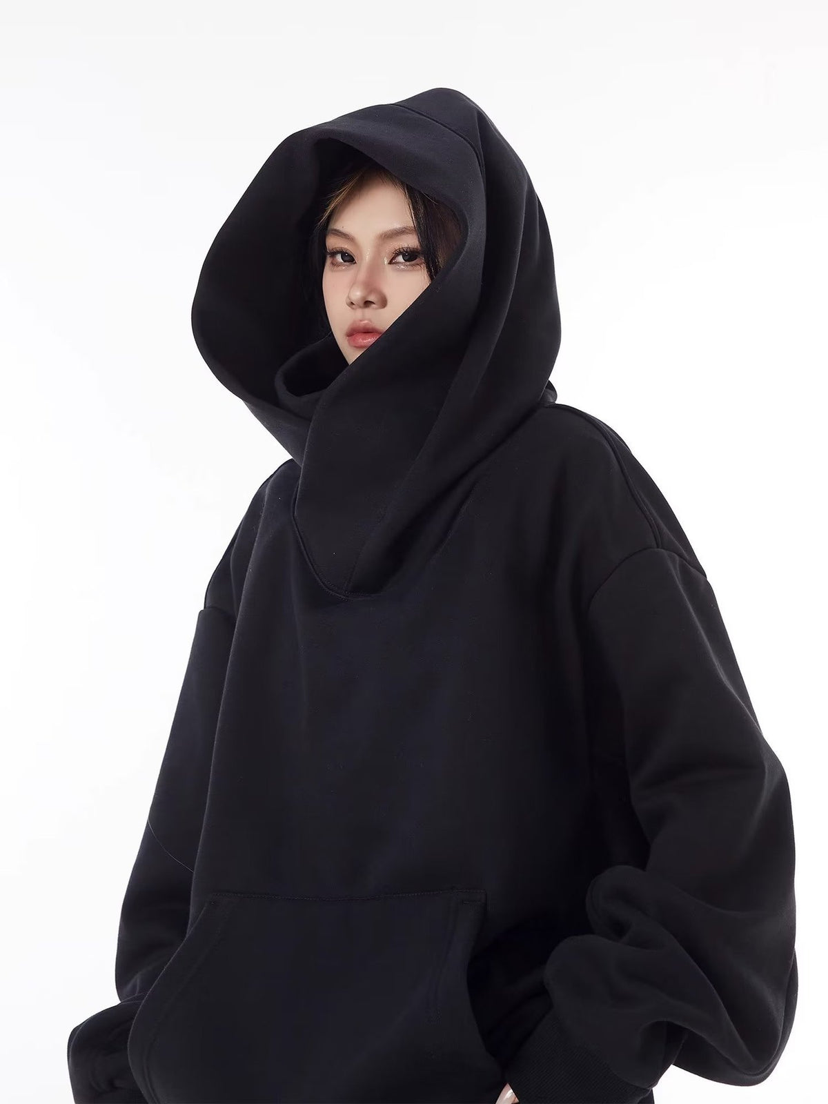 Black oversized hooded sweatshirt with the large hood framing the face and the high collar folded below it