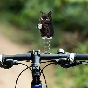 Black cat coffee mug spring ornament bobbing on a bicycle handlebar against a green outdoor blur