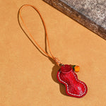 Red peanut shaped leather pendant with a leather cord loop, orange glass bead and stamped tag on a tan background