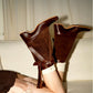 Pair of tan brown foldable boots with a wrap strap and tassel standing on a wood floor