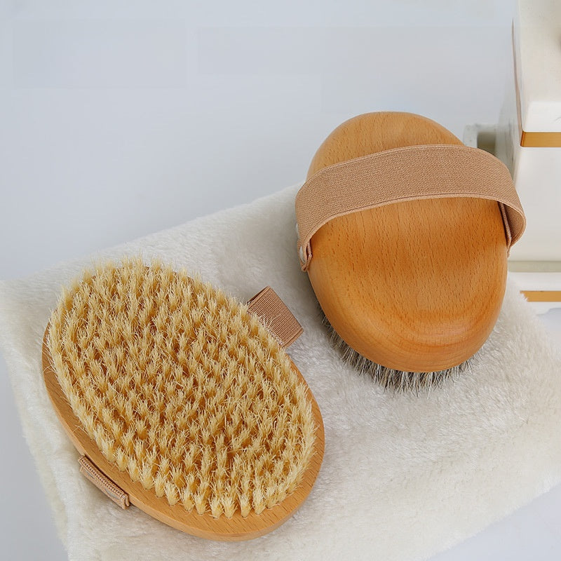 Cream bristle body brush beside a wooden brush back with a beige elastic strap, both on a white towel