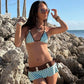 Brown dotted triangle bikini worn by the sea, hip bows knotted at the brown waistband panel