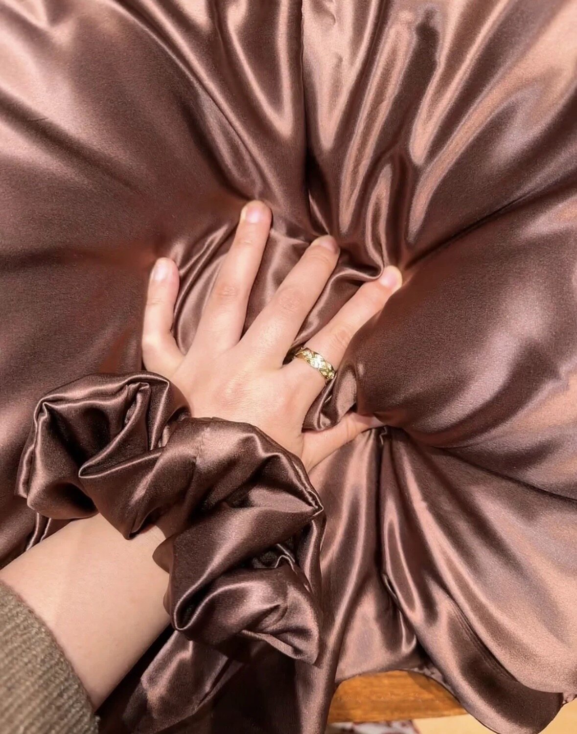 Chocolate slip silk pillowcase gathered under a hand beside a matching scrunchie