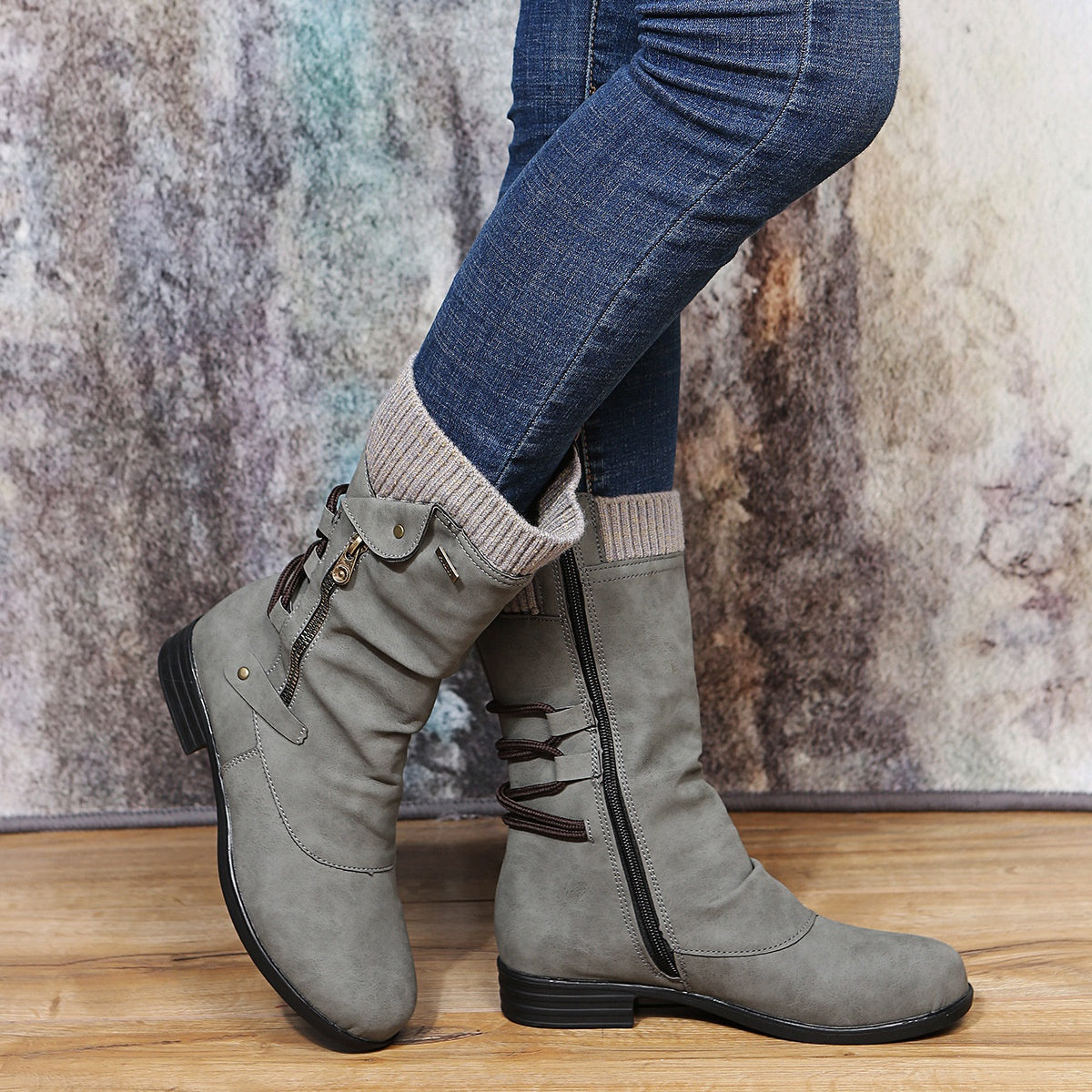 Gray mid calf slouch boots with a knit cuff and an inner side zipper, worn with blue jeans on a wood floor