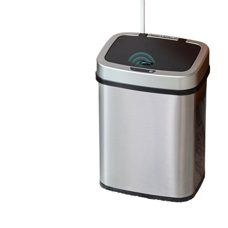 Brushed stainless steel sensor bin beside a low table, black lid with the sensor eye in the centre