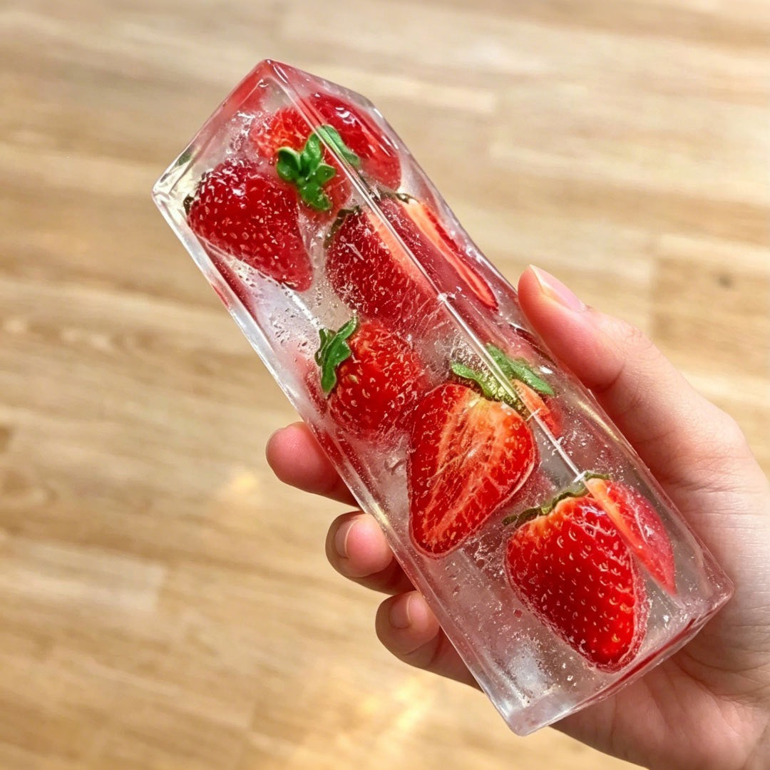 Clear ice cube squishy bar with whole strawberries set inside, held in a hand