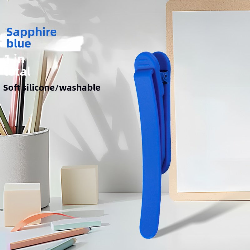 Single sapphire blue silicone bookmark clip standing on a desk beside a pen cup