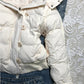 White quilted jacket front with a row of buttons over the zip, a front pocket and a ribbed hem