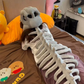 Grey plush dinosaur skeleton head cover without the frame resting on a table by its spine