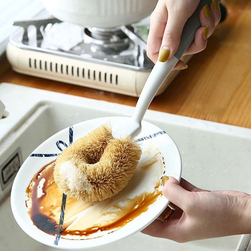 Coconut fiber cleaning brush held in hand over cookware