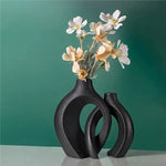 Set of two black nesting ceramic vases with white flowers on a green backdrop