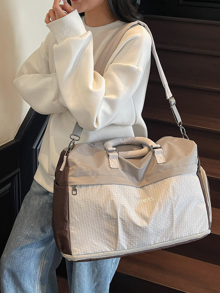 Beige and orange colorblock travel duffel worn on the shoulder with an orange strap on stairs