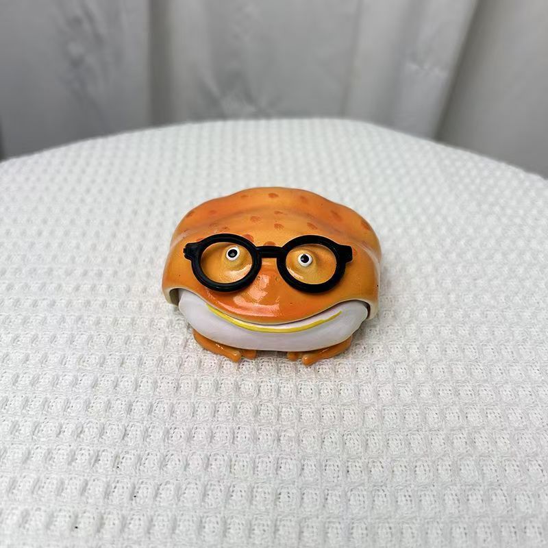 Orange resin frog earbud case wearing round black spectacles, closed, on a white cloth