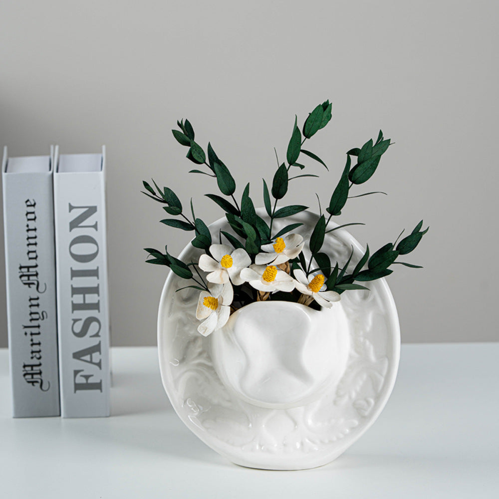 White embossed cowboy hat vase with flowers, styled beside stacked books
