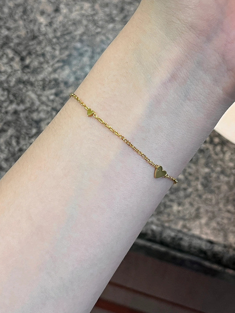 Heart bracelet styled on the wrist beside a sleeve, catching soft daylight