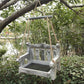 Weathered gray wooden bench bird feeder with a mesh floor and a gray crossbar hanging in a green garden