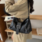 Black soft vegan leather hobo bag with front buckle strap carried on one shoulder with a beige coat