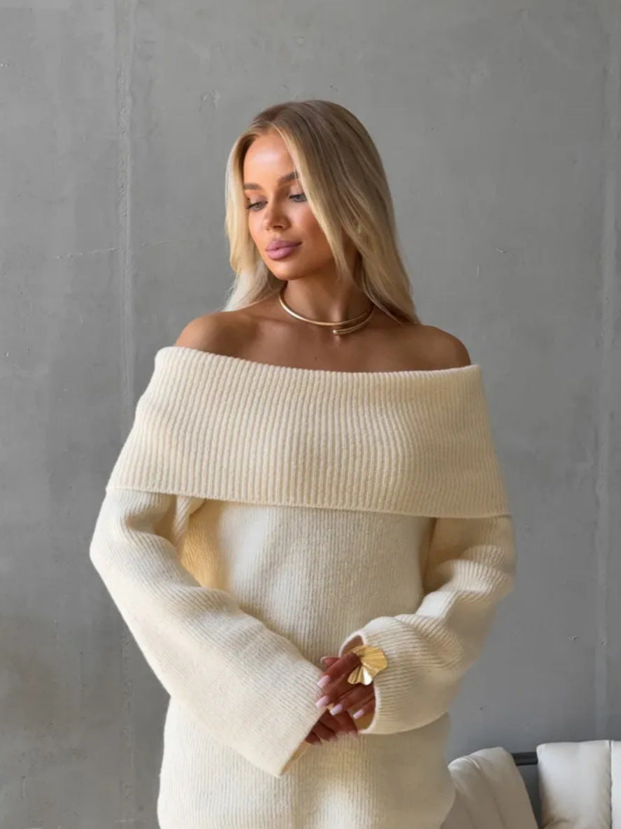 Cream off-shoulder fold-over knit sweater worn with gold jewelry against a concrete wall