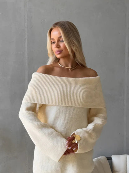Cream off-shoulder fold-over knit sweater worn with gold jewelry against a concrete wall