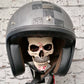 Bone toned resin skull with a mustache under a silver open face helmet on a wall rack