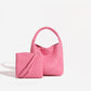 Bright pink plaited PU bucket bag with the woven zip pouch and its wrist loop standing in front