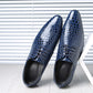 Pair of blue croc embossed derby shoes with pointed toes, black lining and laces, leaning on a white hexagon