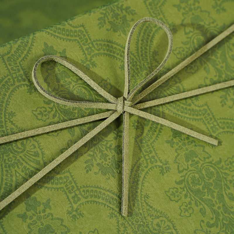 Close-up of a cord bow tied on the damask-patterned lid of an olive green gift box
