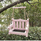 Pink wooden bench bird feeder with a mesh floor and a pink crossbar hanging in a green garden