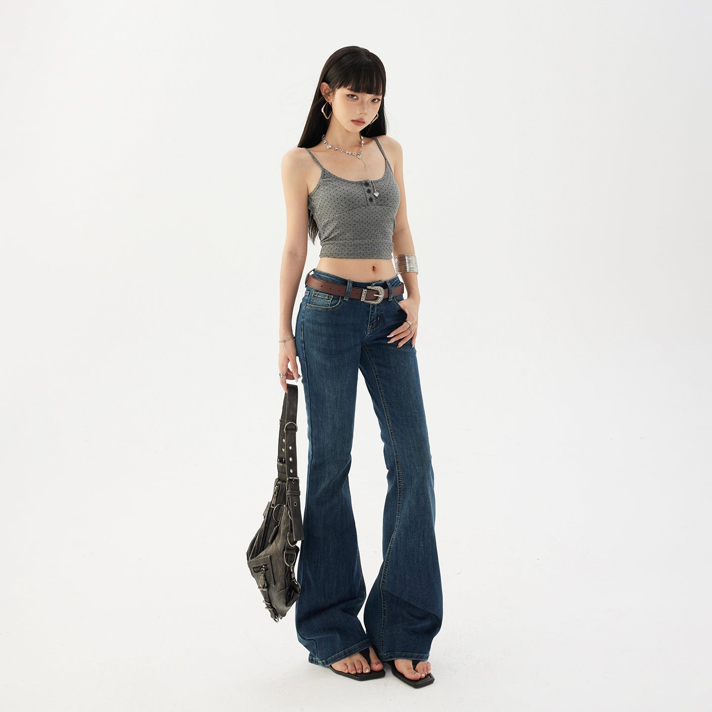 Low rise flared jeans on a model styled with a brown belt and a shoulder bag, front view