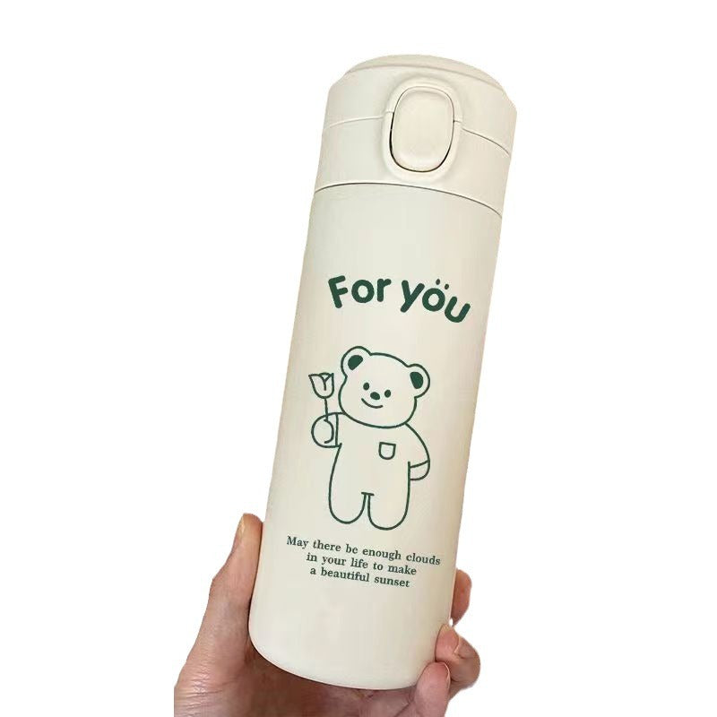 Cream insulated bottle on white, green bear drawing, flip top button visible on the collar