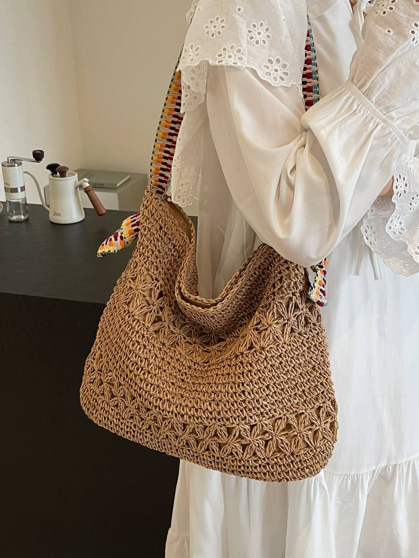 Khaki woven straw shoulder bag with colorful strap held at the side indoors