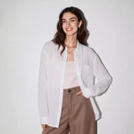 Woman wearing a lightweight white linen button-up shirt open over a cami with brown trousers