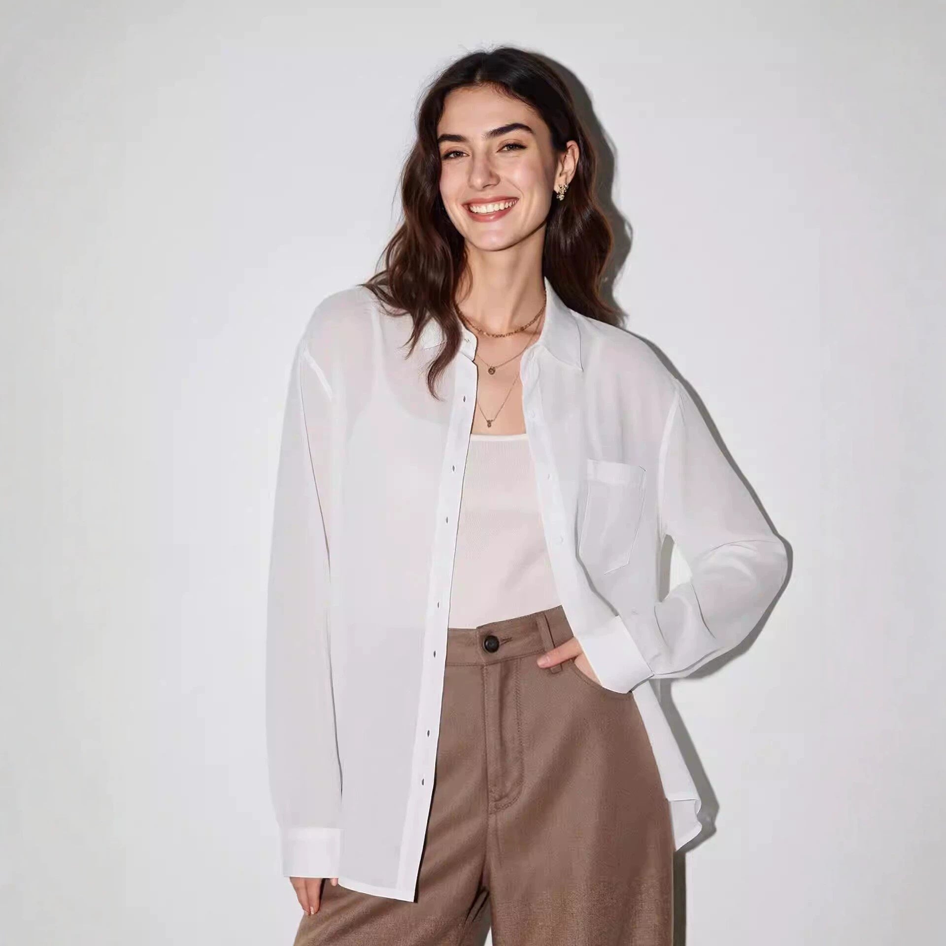 Woman wearing a lightweight white linen button-up shirt open over a cami with brown trousers