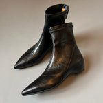 Pair of black pointed toe ankle boots with a back zip and a wedge heel on a grey background