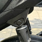 Black plastic cover over a motorcycle rear shock absorber mount, beaded with rain drops
