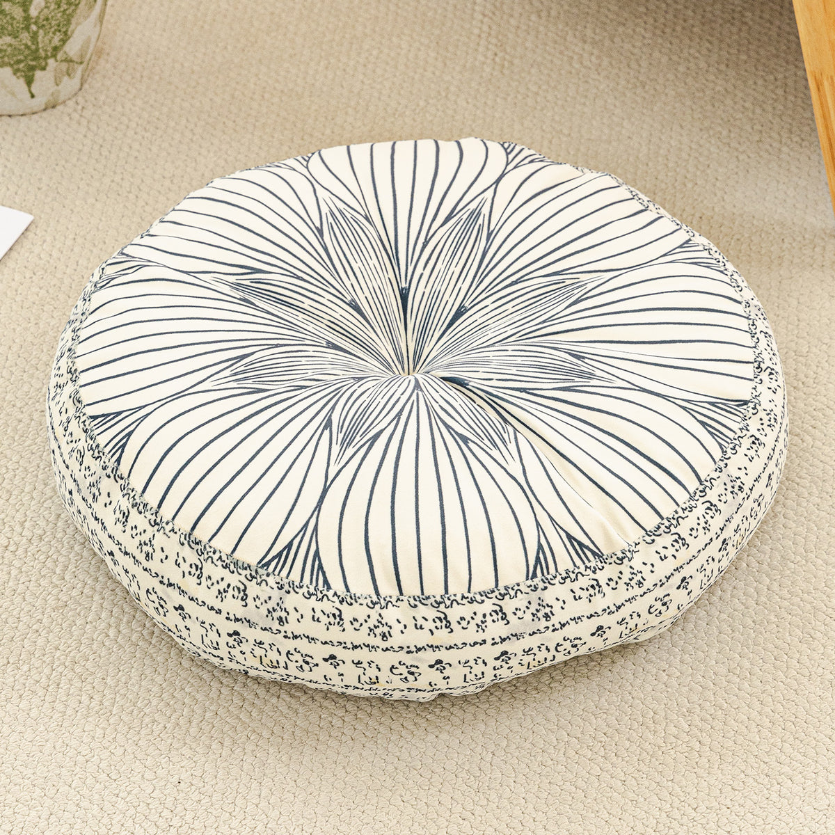 Round cushion with a navy line sunburst print on a cream top and a navy patterned side, on a beige rug