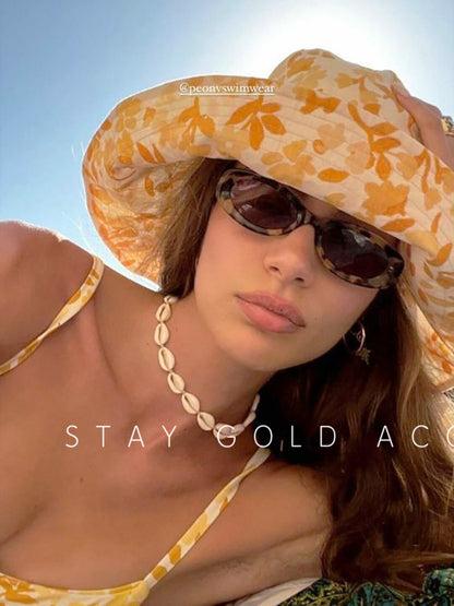 Woman on a beach wearing the cowrie shell choker on cream cord under a wide brimmed sun hat