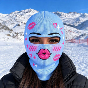 Model in a light blue printed balaclava with pink lips, hearts and sparkles in front of snowy mountains