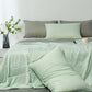 Pale green summer coverlet spread across a made bed with grey and green pillows behind