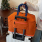 Back of the orange travel duffel showing the trolley sleeve over a suitcase handle
