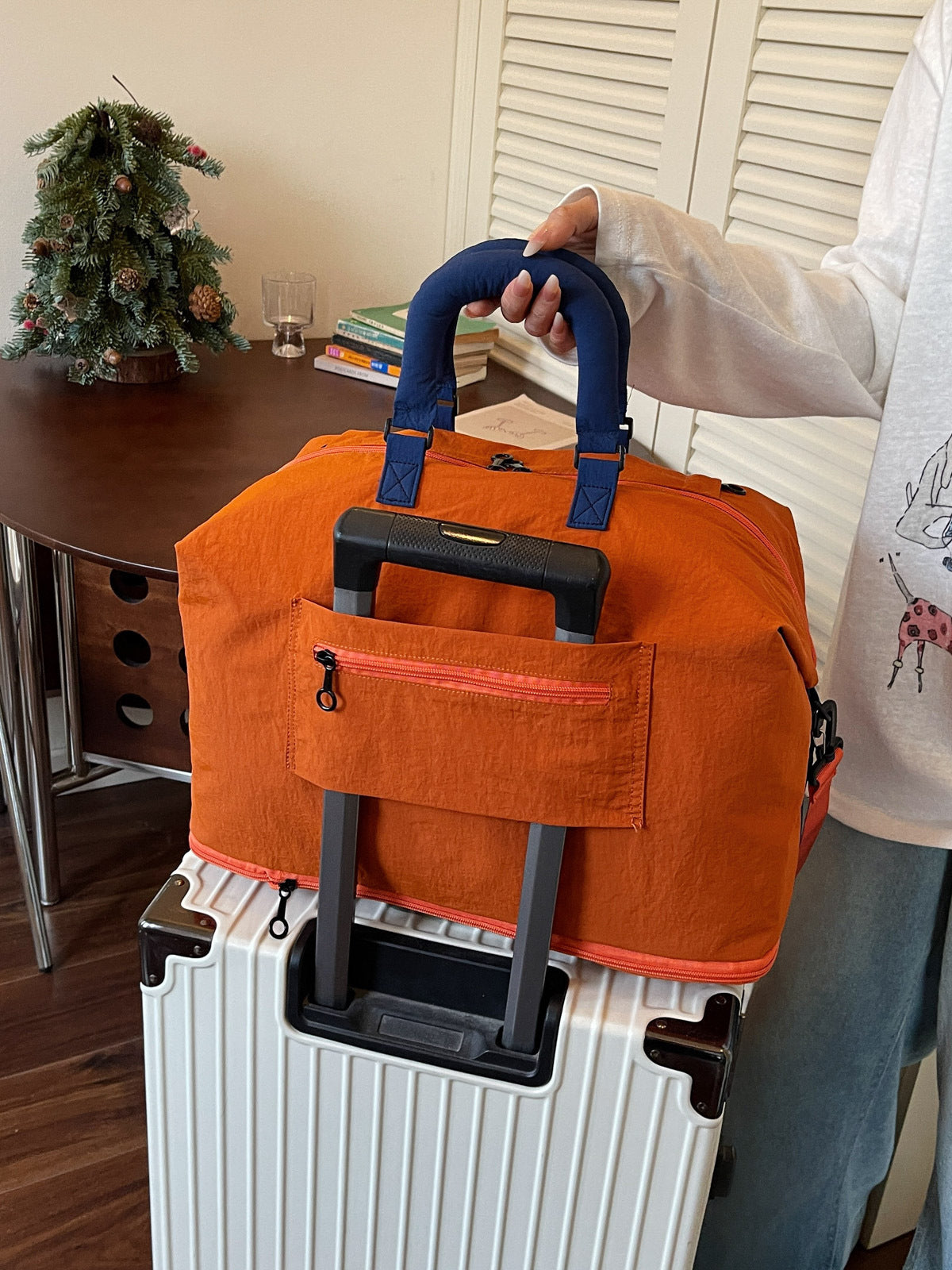 Back of the orange travel duffel showing the trolley sleeve over a suitcase handle