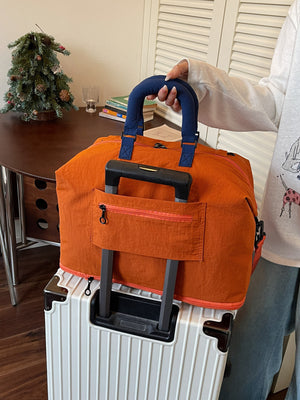 Back of the orange travel duffel showing the trolley sleeve over a suitcase handle