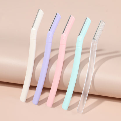 Five eyebrow razors in white, lilac purple, pink, mint green and frosted transparent leaning on a peach backdrop