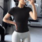 Woman in a black fitted short sleeve fitness T-shirt with light gray shorts in a gym, front view
