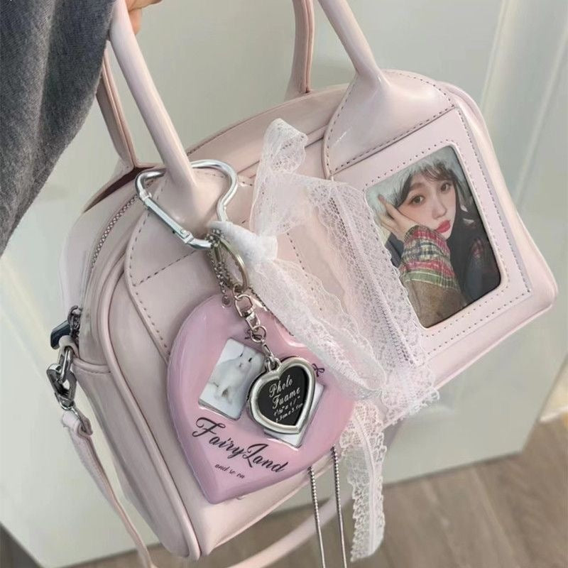 Pink card window crossbody bag held by its handles with the detachable strap clipped to the side