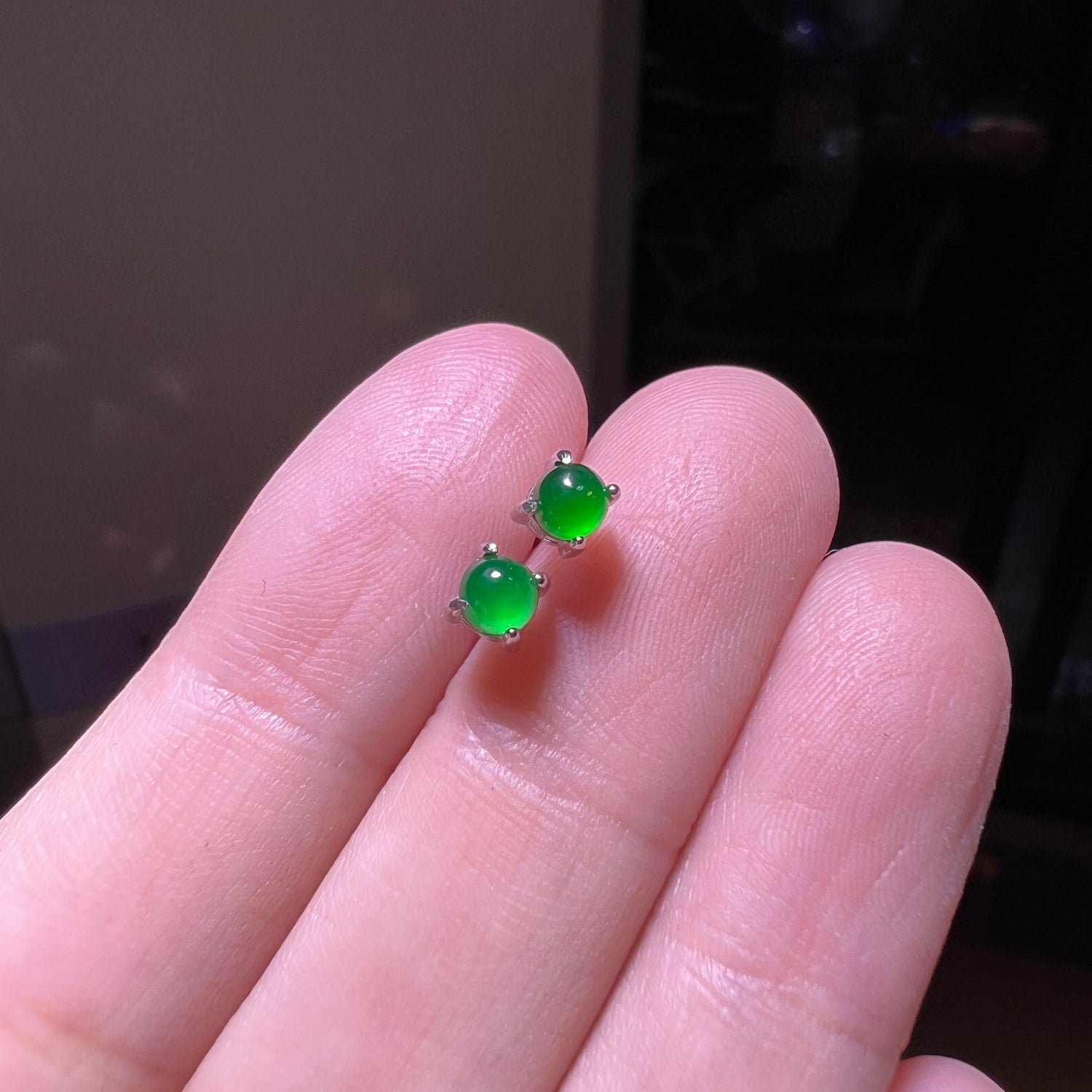 Close macro of a saturated green cabochon stud in a bright silver tone claw setting on fingertips