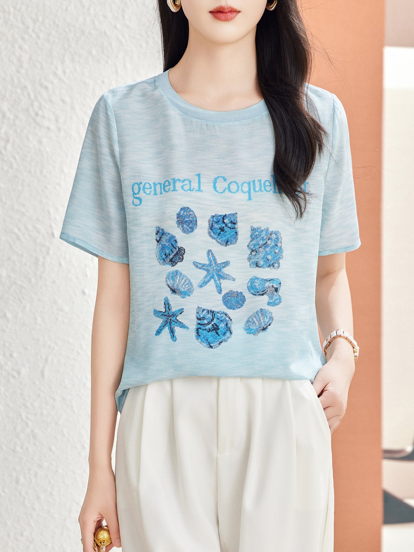 Woman in Lake Blue silk blouse with woven seashell and starfish motif on the chest